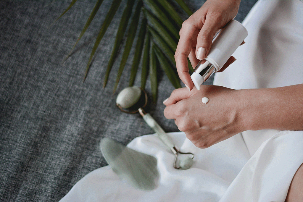Flatlay of hands applying a drop of moisturizer on the skin, with jade rollers and palm leaves—capturing Pneumera’s natural skincare ritual.